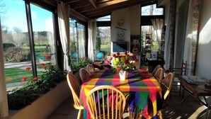 Un coin repas avec une table ronde recouverte d’une nappe colorée, entourée de chaises en bois.