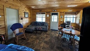 L’intérieur d’un chalet en bois, avec un canapé, une table à manger et un ventilateur de plafond.
