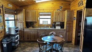 Une cuisine rustique, située dans une cabane en bois, avec une table à manger ronde, des placards en bois et un réfrigérateur.