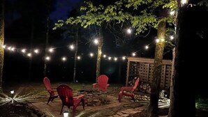 Un espace extérieur aménagé en terrasse, avec des chaises rouges, des guirlandes lumineuses et un foyer en pierre.