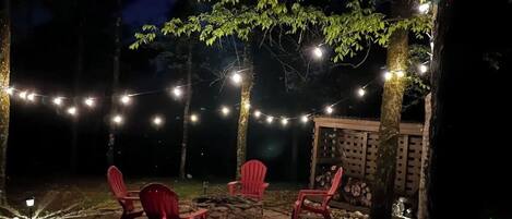 An outdoor patio area with red chairs, string lights, and a stone fire pit.