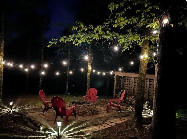 An outdoor patio area with red chairs, string lights, and a stone fire pit.