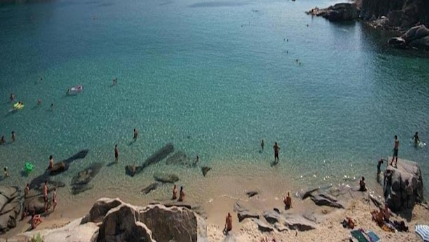 Une plage avec une eau claire, des rochers et des gens qui se baignent.
