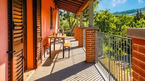 Un balcon agrémenté d’une pergola en bois, une table avec des chaises et une vue sur la verdure et les collines.