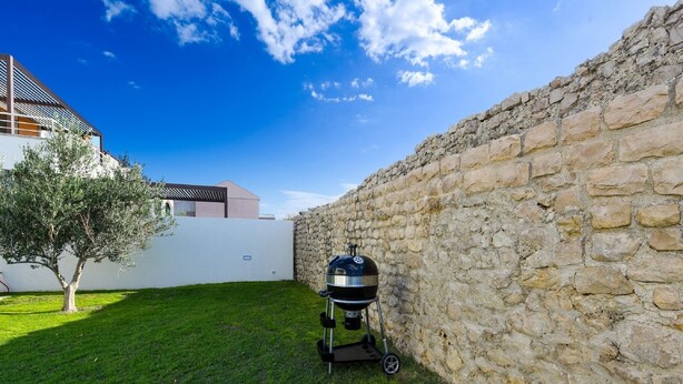 Un jardin avec un mur en pierre, un barbecue et un arbre.