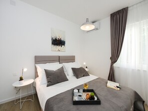 Quarto moderno com cama, mesas de cabeceira, um quadro e uma bandeja de café da manhã.