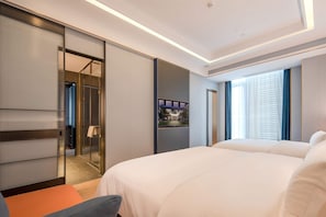 Habitación de hotel moderna con una cama grande, zona de estar, baño con paredes de vidrio y vistas al exterior.