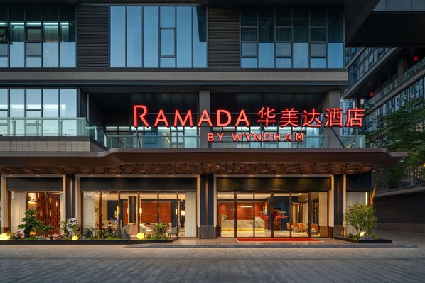 Une entrée d’hôtel moderne, avec une grande enseigne indiquant « RAMADA » et « BY WYNDHAM ».