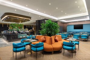 Un espace lounge moderne avec un canapé orange central, des fauteuils bleus et un comptoir de bar.