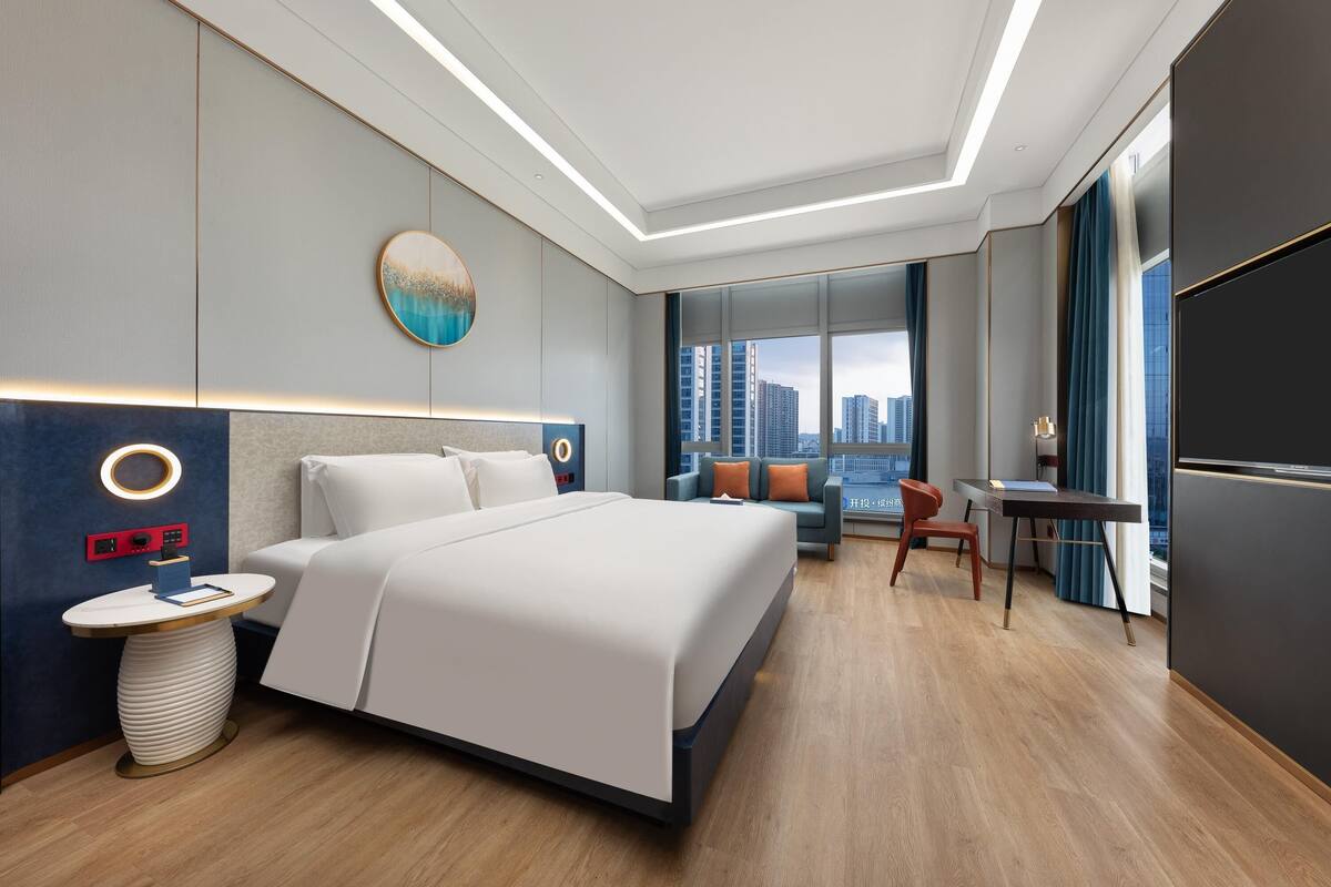 A modern hotel room with a large bed, a desk, and a view of the city.
