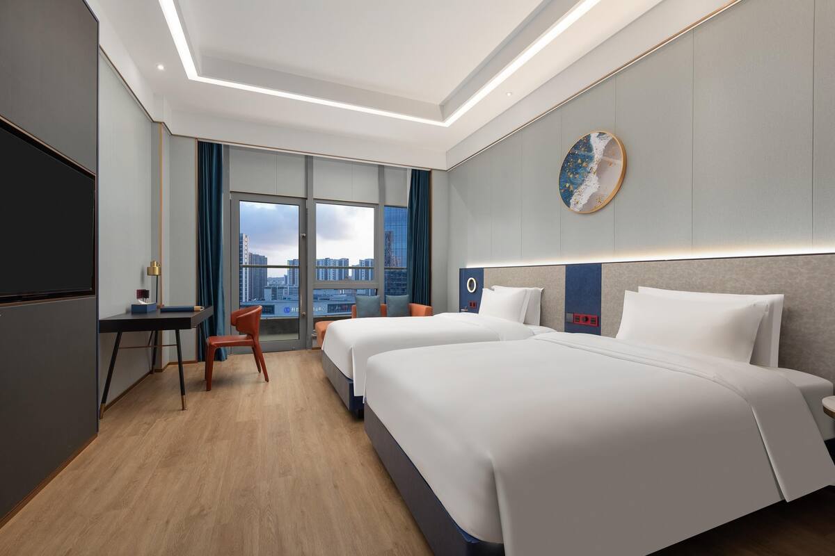 A modern hotel room with two beds, a desk, and a chair.
