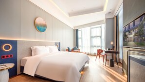 A modern hotel room with a large bed, a desk, a chair, and a view of the city through large windows. - Ramada BY Wyndham Guangzhou Huangpu (Guangzhou)