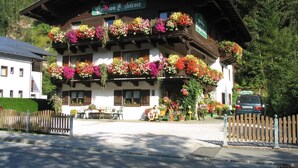 Ein traditionelles Gebäude im alpinen Stil mit mehreren Balkonen, die mit bunten Blumen geschmückt sind, einem Schild, das es als Restaurant kennzeichnet, und einem Holzzaun im Vordergrund.