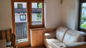 Ein Zimmer mit Holzboden, einem beigen Sofa, einem Holztisch und einem Fenster mit Blick auf einen Balkon.