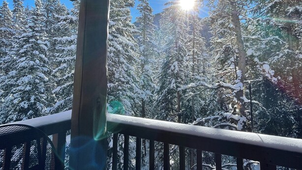 A snowy forest with a sunlit sky, a wooden deck, and a railing. - Spacious and Bright Keystone Townhome (Keystone)