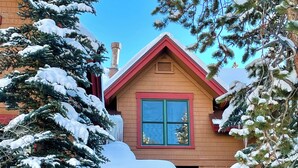 A two-story wooden house with a red roof and a balcony. Snow covers the trees and ground. - Spacious and Bright Keystone Townhome (Keystone)