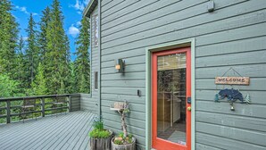 Une terrasse en bois avec une porte rouge, une pancarte de bienvenue et une décoration représentant un ours.