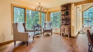 Une pièce spacieuse dotée de grandes fenêtres, de deux fauteuils, d’une bibliothèque en bois et d’un lustre.