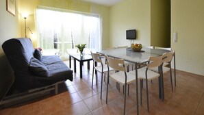 A dining area with a table, chairs, a sofa, a TV, and a window with curtains. - Küstenwohnung in Zierow (Zierow)