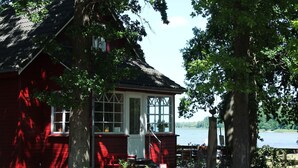 A red wooden house with a porch, a small deck, and a view of a lake. - Küstenwohnung in Zierow (Zierow)