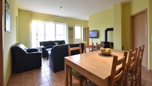 A dining area with a wooden table and chairs, a television mounted on the wall, and a window with curtains. - Komfortables Wohnung in Zierow mit Sauna (Zierow)