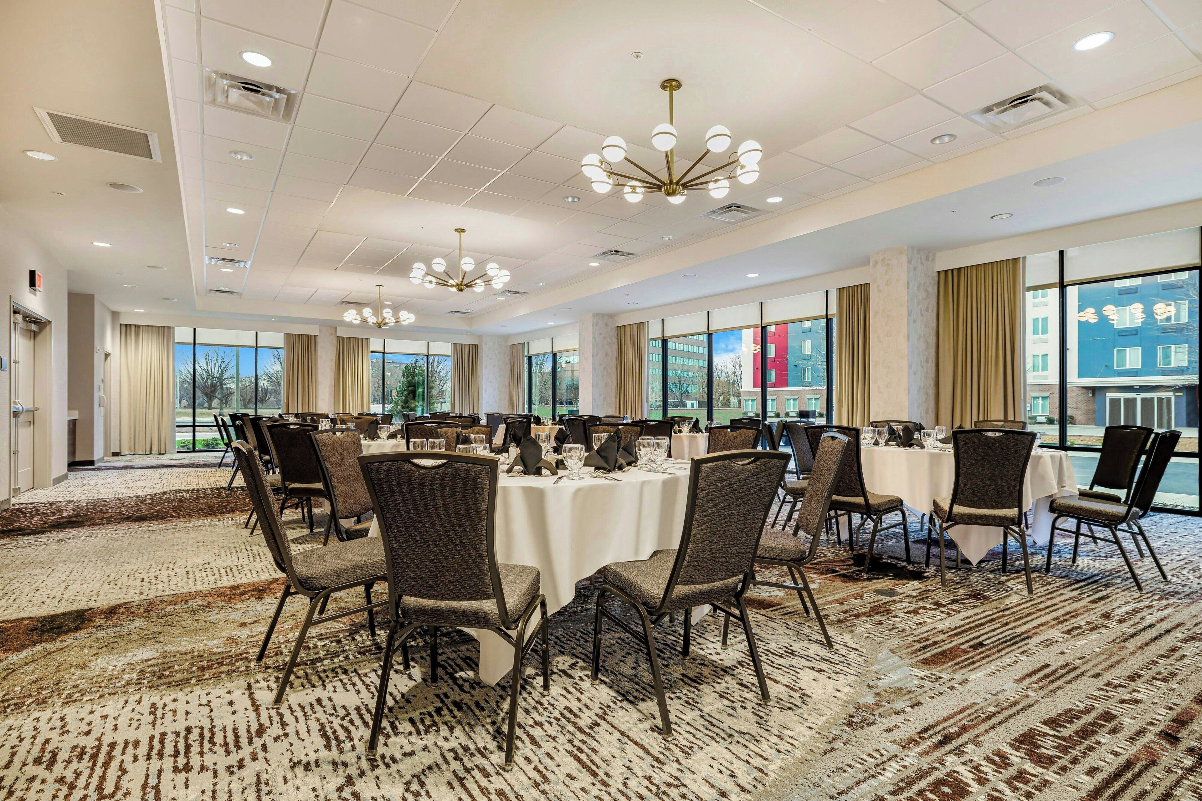 A spacious conference room with round tables and chairs, large windows, and a patterned carpet.