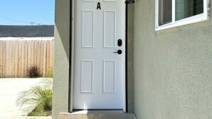 A white door with the letter 'A' above it, a small step leading up to the door, and a window to the right.