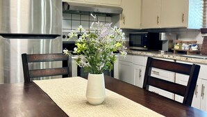 A kitchen with white cabinets, a stainless steel refrigerator, a microwave, and a vase with flowers on the dining table.