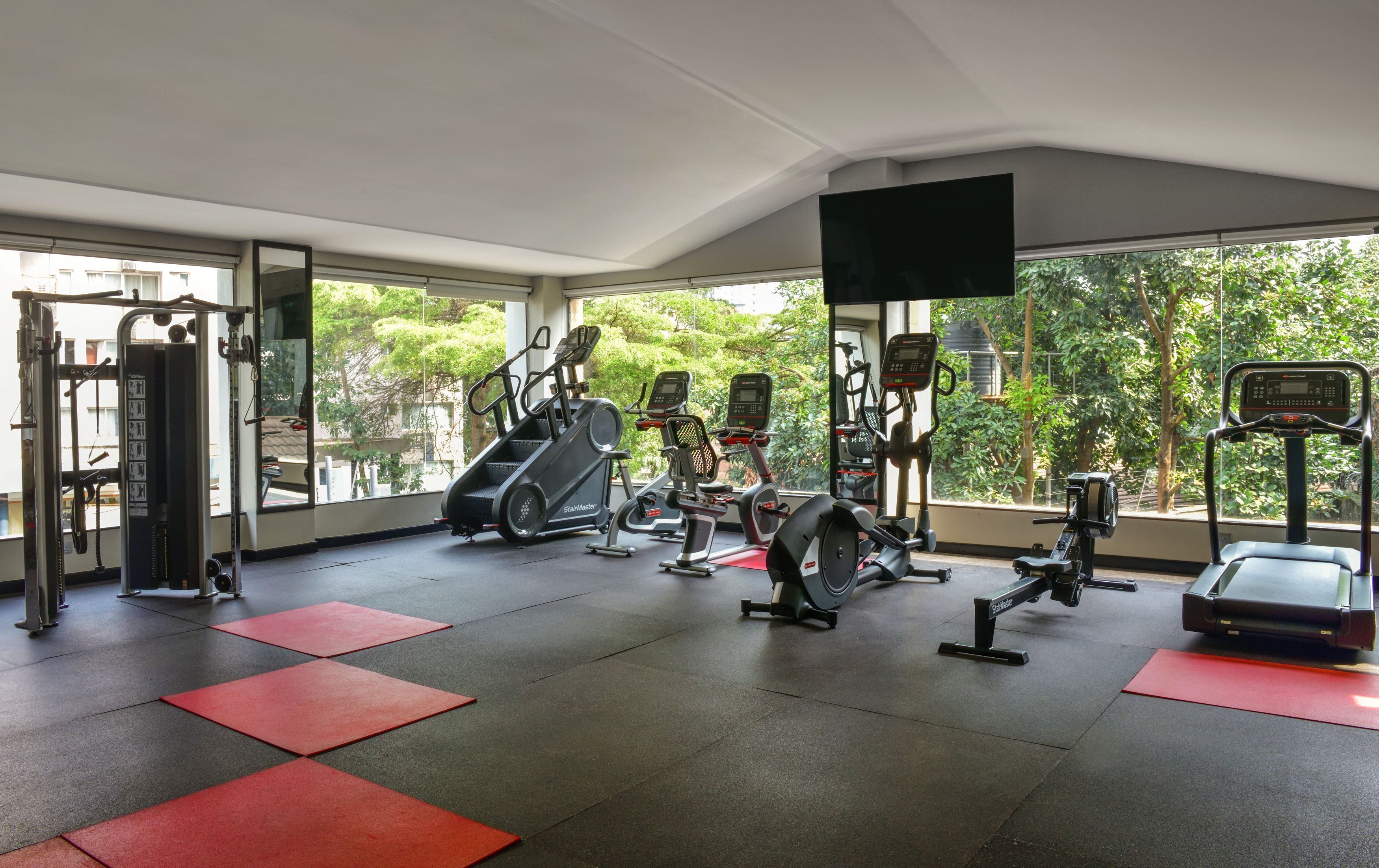 A gym with various exercise equipment, including treadmills and weight machines, and red mats on the floor.