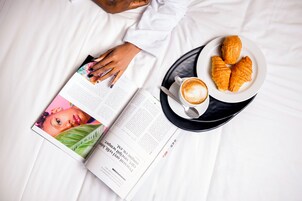 Un libro, un plato con cruasanes y una taza de café sobre la cama.