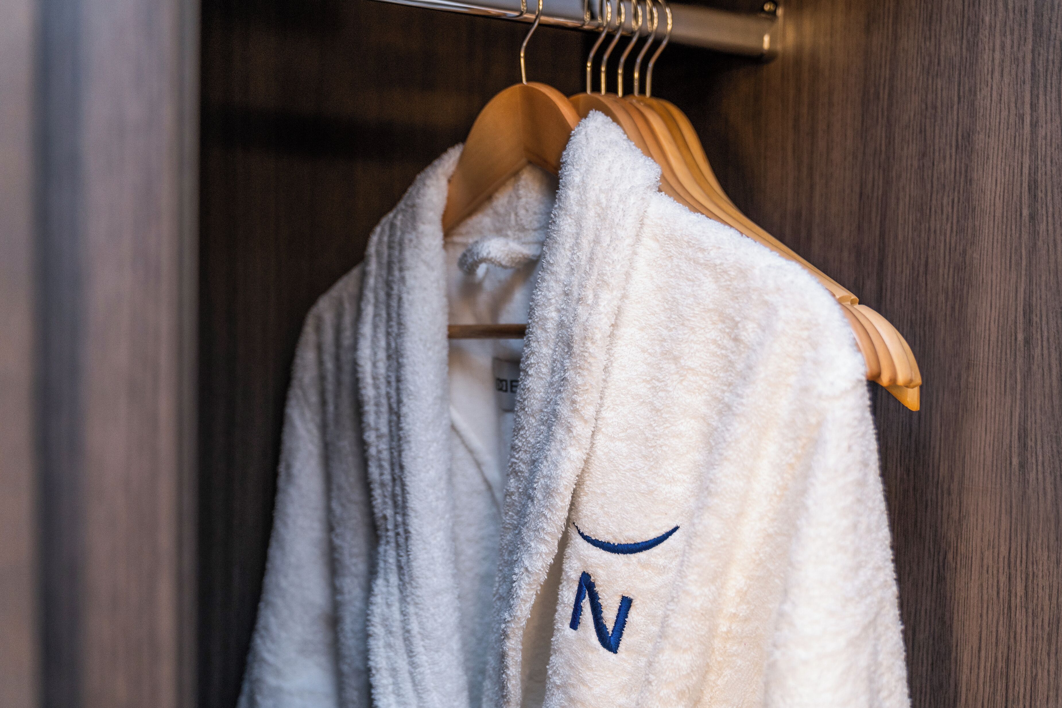 A white robe with a blue 'N' hanging on a wooden hanger in a closet.