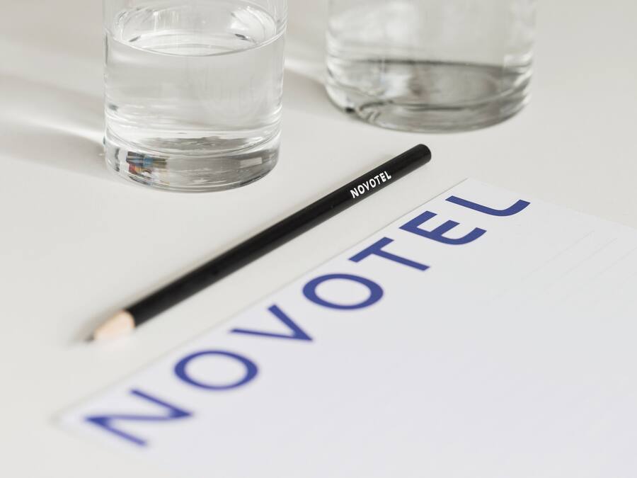 Un vaso transparente con agua, un bolígrafo negro que dice NOVOTEL y un papel con la palabra NOVOTEL impresa.