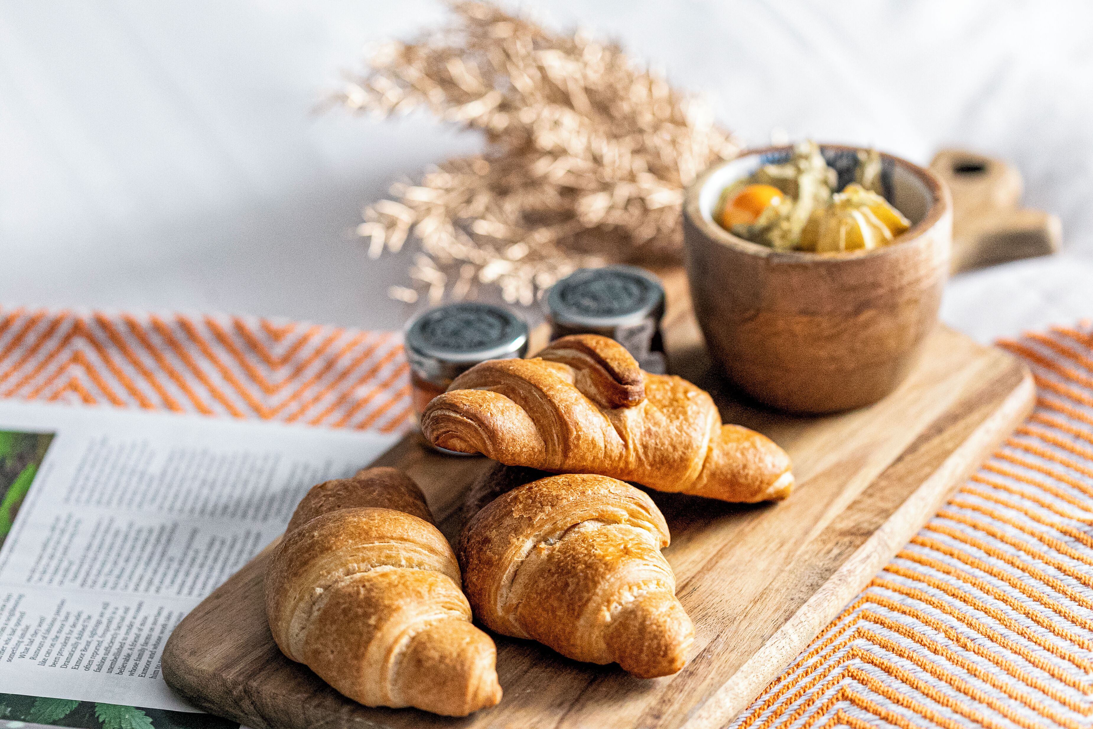 Croissants on a wooden board, a bowl of fruit, and salt and pepper shakers.