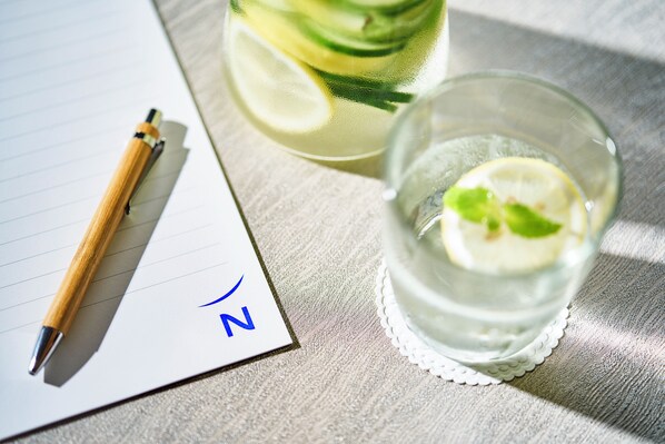 Un bloc de notas con un bolígrafo, un vaso de agua con rodajas de limón y una botella de agua sobre una superficie rugosa.