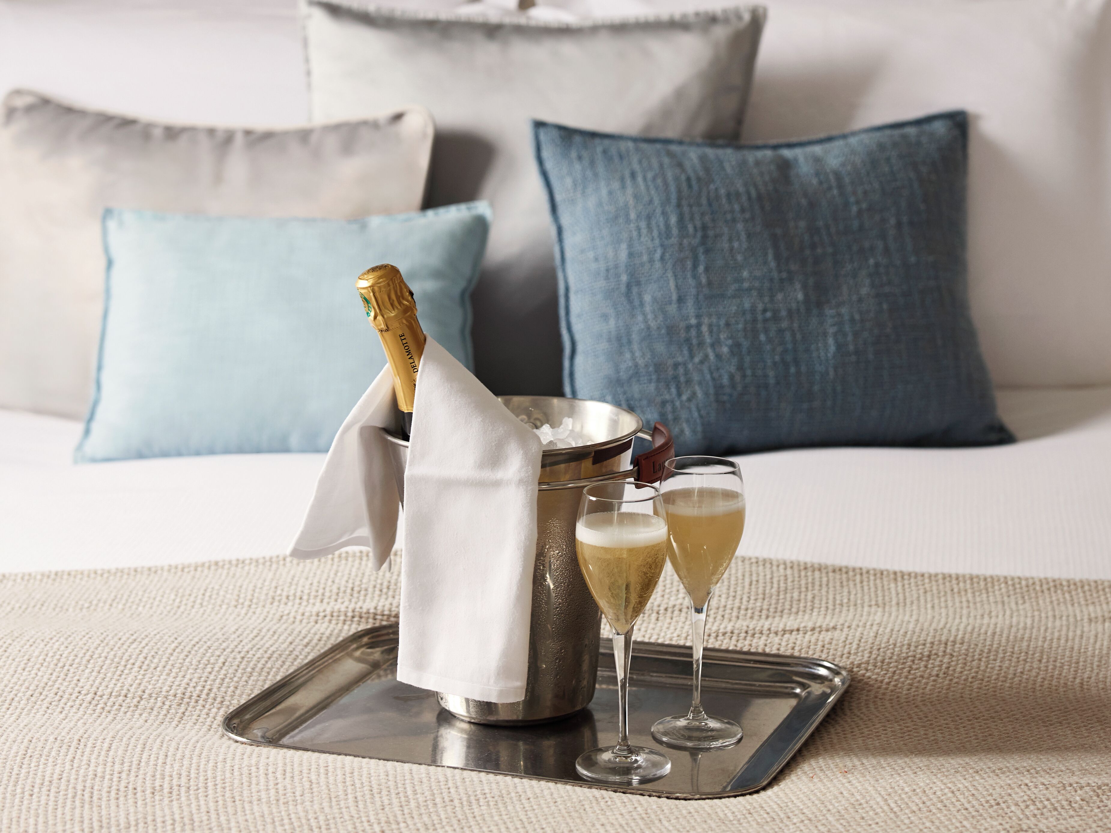 A tray with a champagne bottle, two glasses of champagne, and a metal bucket on a textured surface.