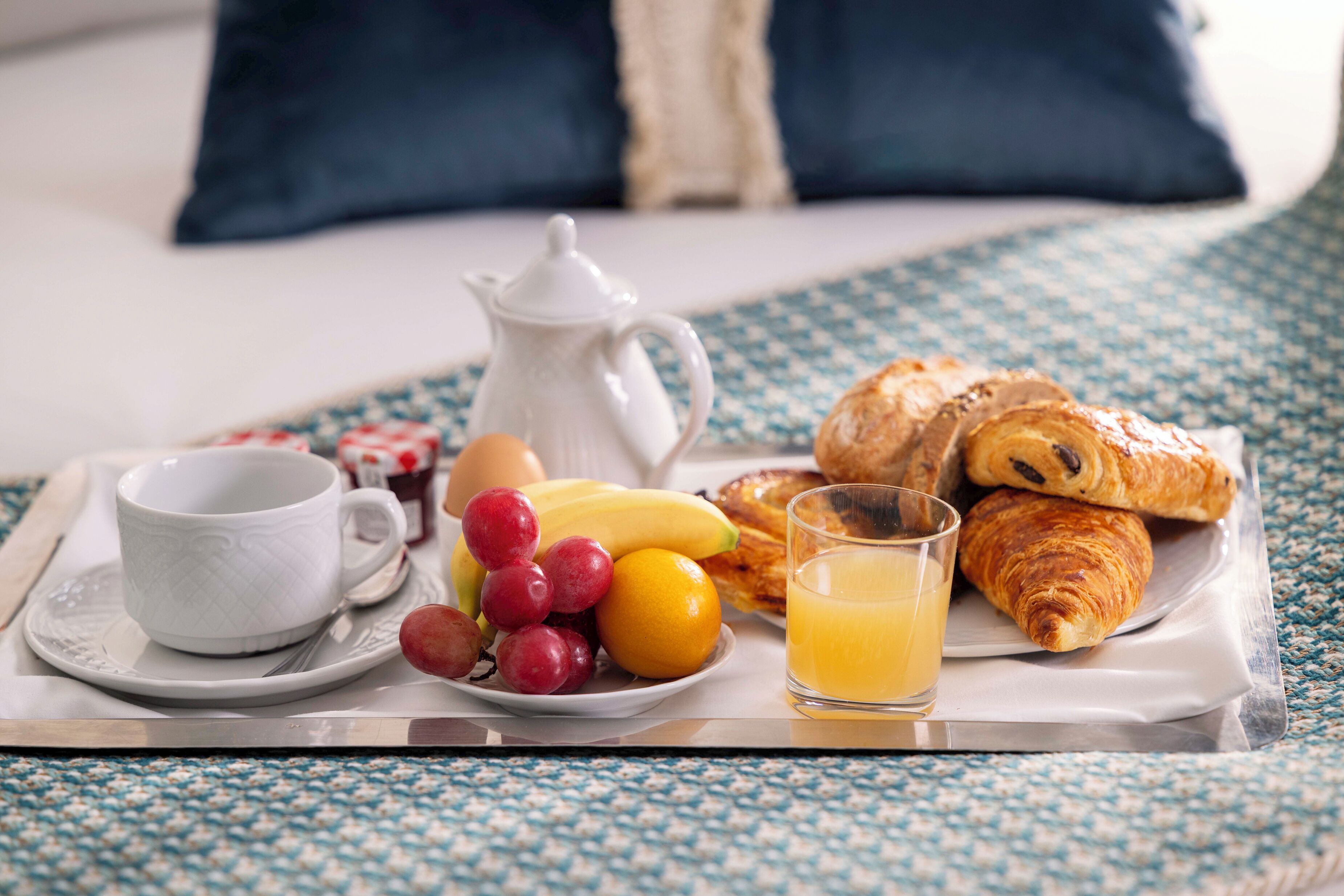 A breakfast tray with croissants, a cup, a jug, a plate with fruit, and a glass of orange juice.
