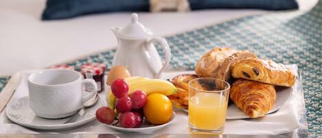 A breakfast tray with croissants, a cup, a jug, a plate with fruit, and a glass of orange juice.