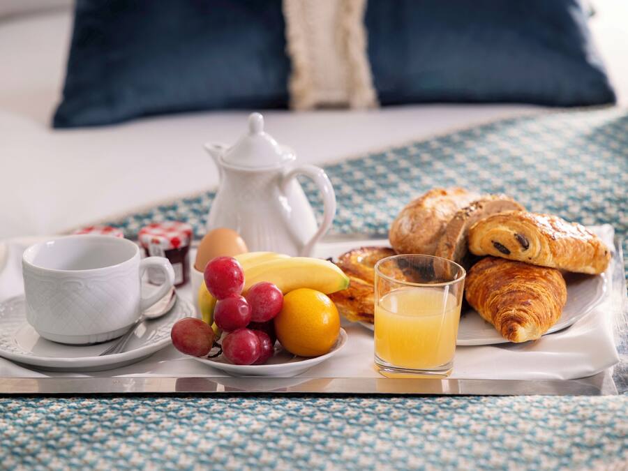 Ein Frühstücksbrett mit Croissants, einer Tasse, einer Karaffe, einem Teller mit Obst und einem Glas Orangensaft.