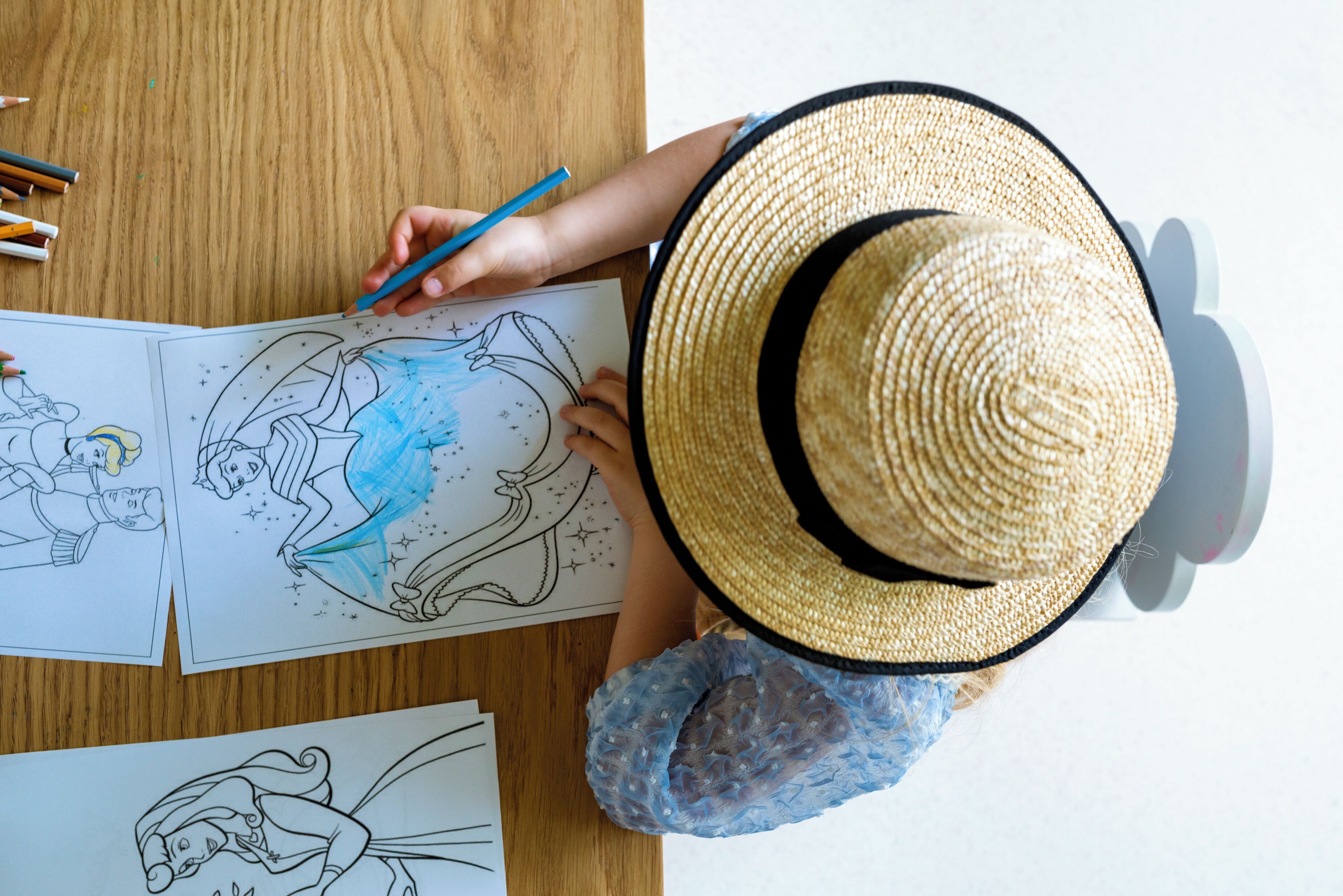 A person coloring a drawing on a wooden table with various colored pencils.