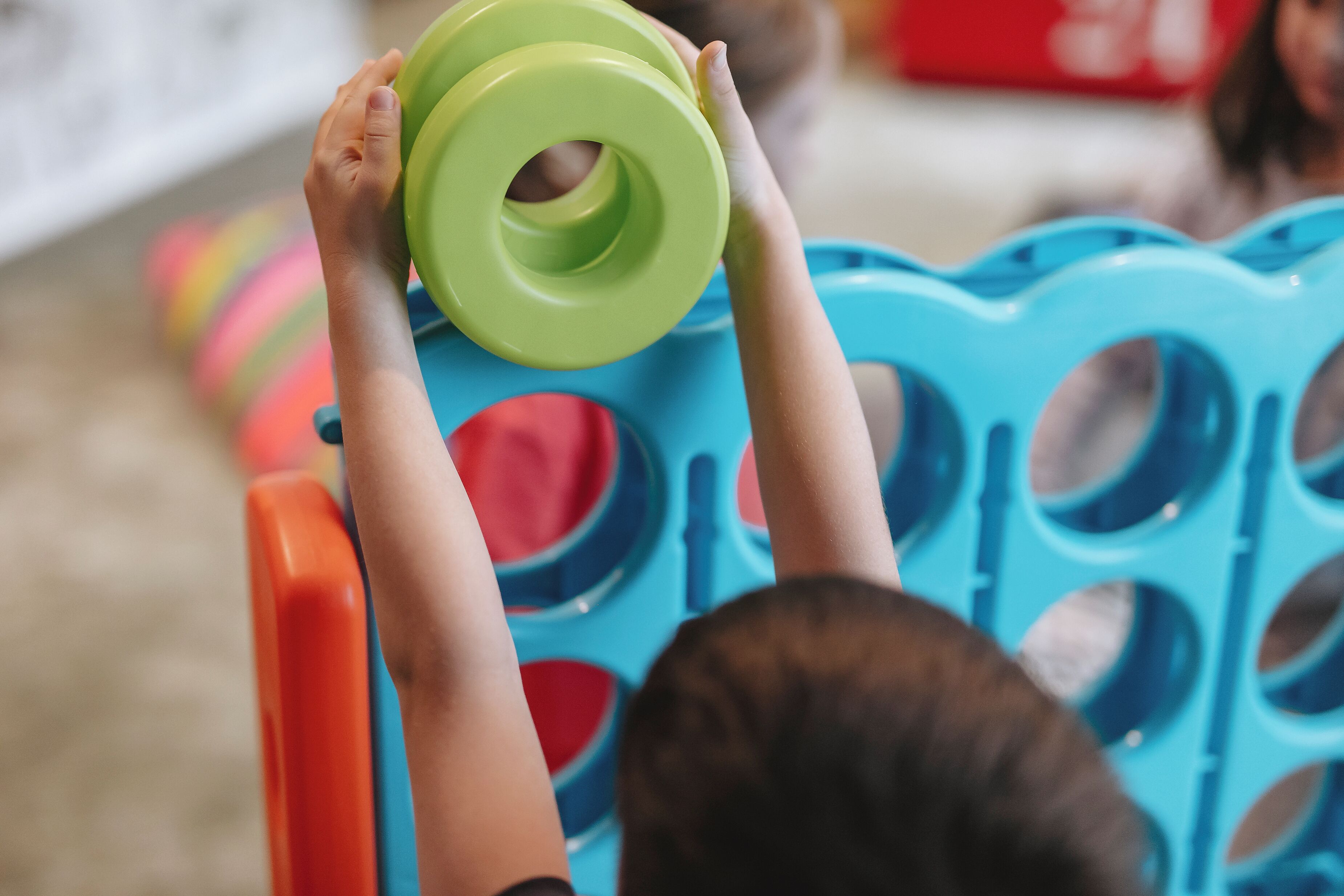 A child holding a green object above a blue structure with circular cutouts.