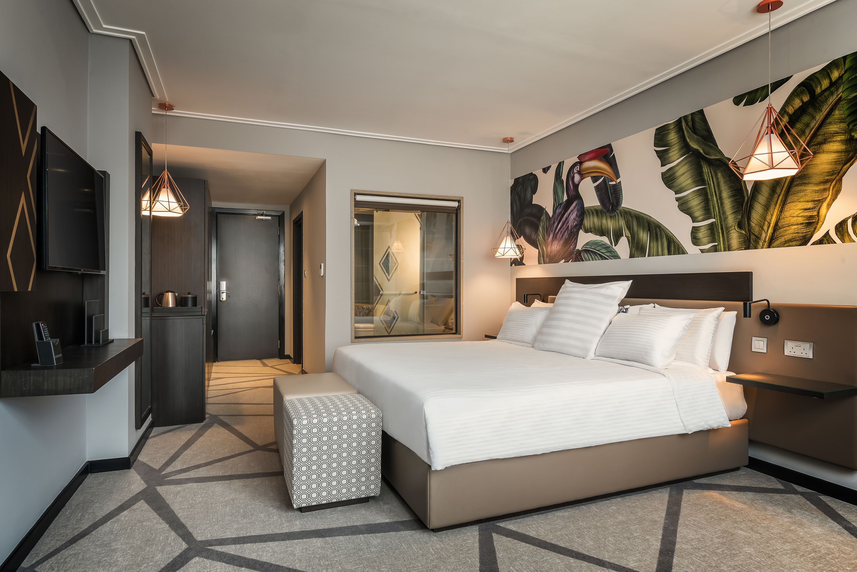 Une chambre d’hôtel moderne, dotée d’un grand lit, d’une télévision, d’un bureau et d’une salle de bain visible à travers une porte ouverte.