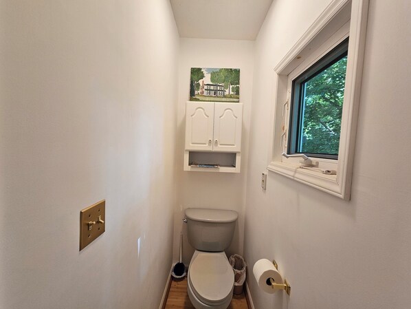 A small, narrow bathroom with a toilet, a window, and a wall-mounted cabinet.