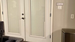 Um quarto com uma porta dupla, uma lixeira e uma tomada na parede.