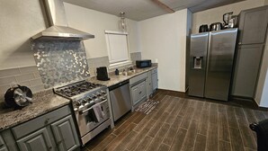 Uma cozinha moderna com eletrodomésticos de aço inoxidável, bancadas de granito e painel de azulejos em padrão herringbone.