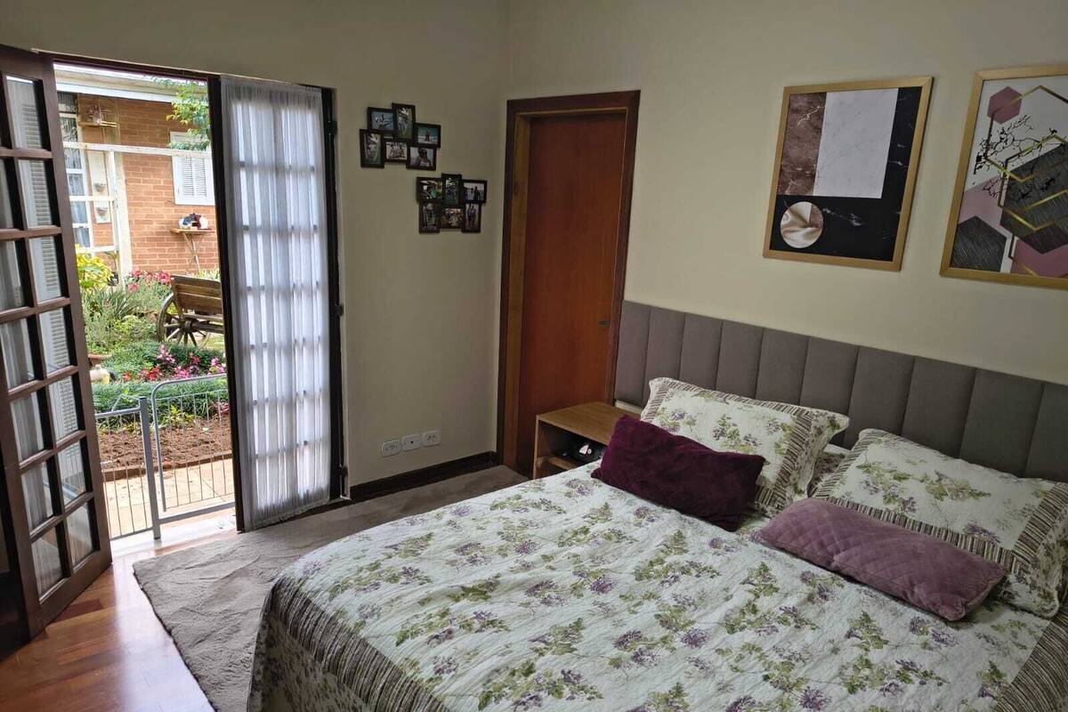 Une chambre à coucher avec un lit, une table de chevet en bois, une porte et une fenêtre avec des stores.