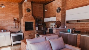 Una sala de estar acogedora con chimenea de ladrillo, un sofá y una cocina con armarios blancos y pared de ladrillo.