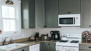 A kitchen with green cabinets, a white microwave, a stove, and a wooden table with a bowl.