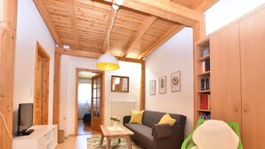 A cozy living room with a wooden ceiling, a grey sofa, a white TV stand, and a green chair. - Ferienwohnung in Rerik bis zu 2 Personen (Rerik (Ostseebad))