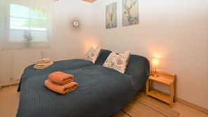 A bedroom with a bed, two pillows, a bedside table, a lamp, a mirror, and wall art. - Ferienwohnung in Rerik bis zu 2 Personen (Rerik (Ostseebad))