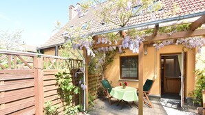 A covered patio with a table and chairs, a wooden fence, and a building with a tiled roof. - Ferienwohnung in Rerik bis zu 2 Personen (Rerik (Ostseebad))